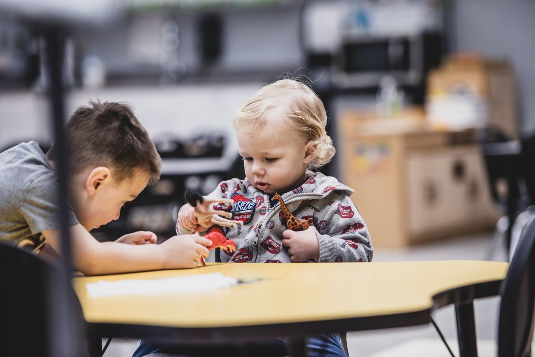 Two young children at a yellow table during snack
