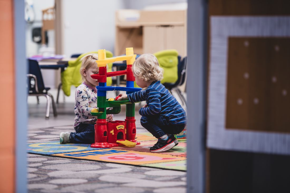 Two toddlers stack colourful ring towers on a classroom rug