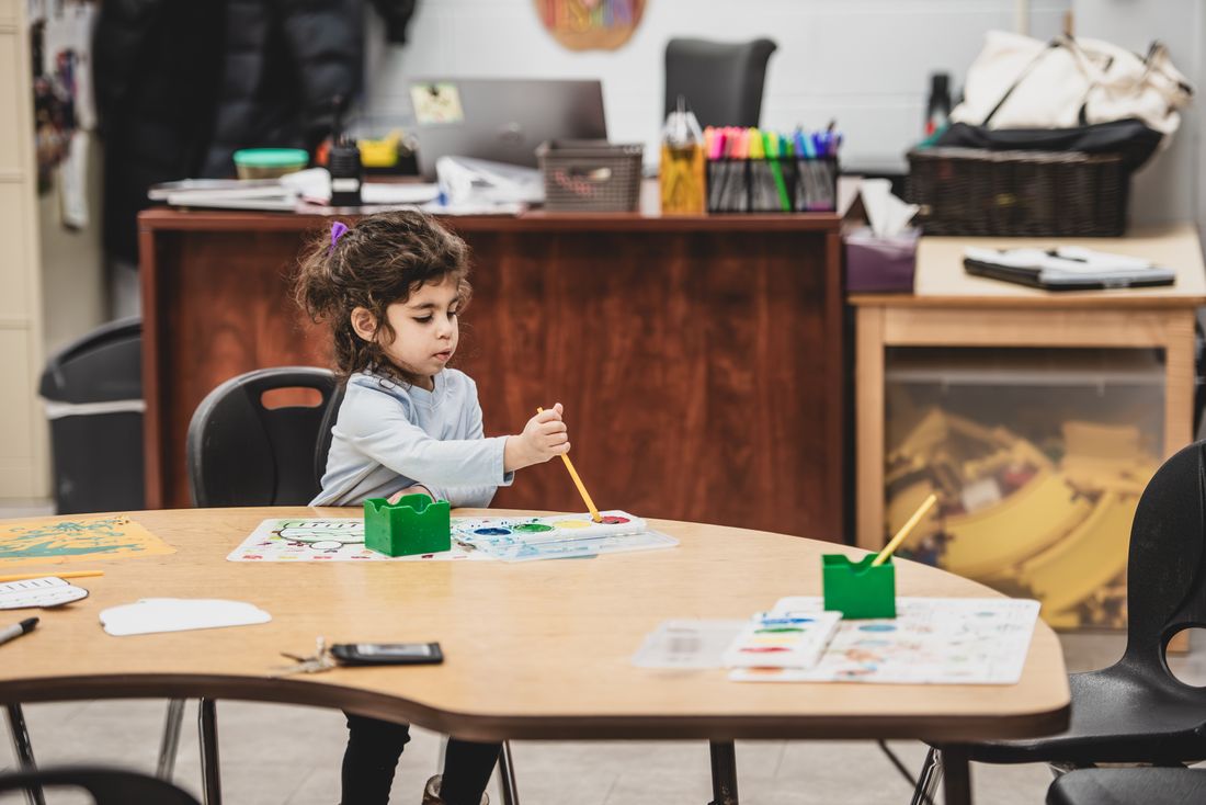 A preschooler paints with a brush at a table