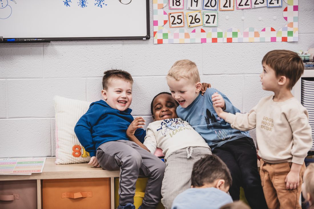 Four boys laugh together on a classroom bench