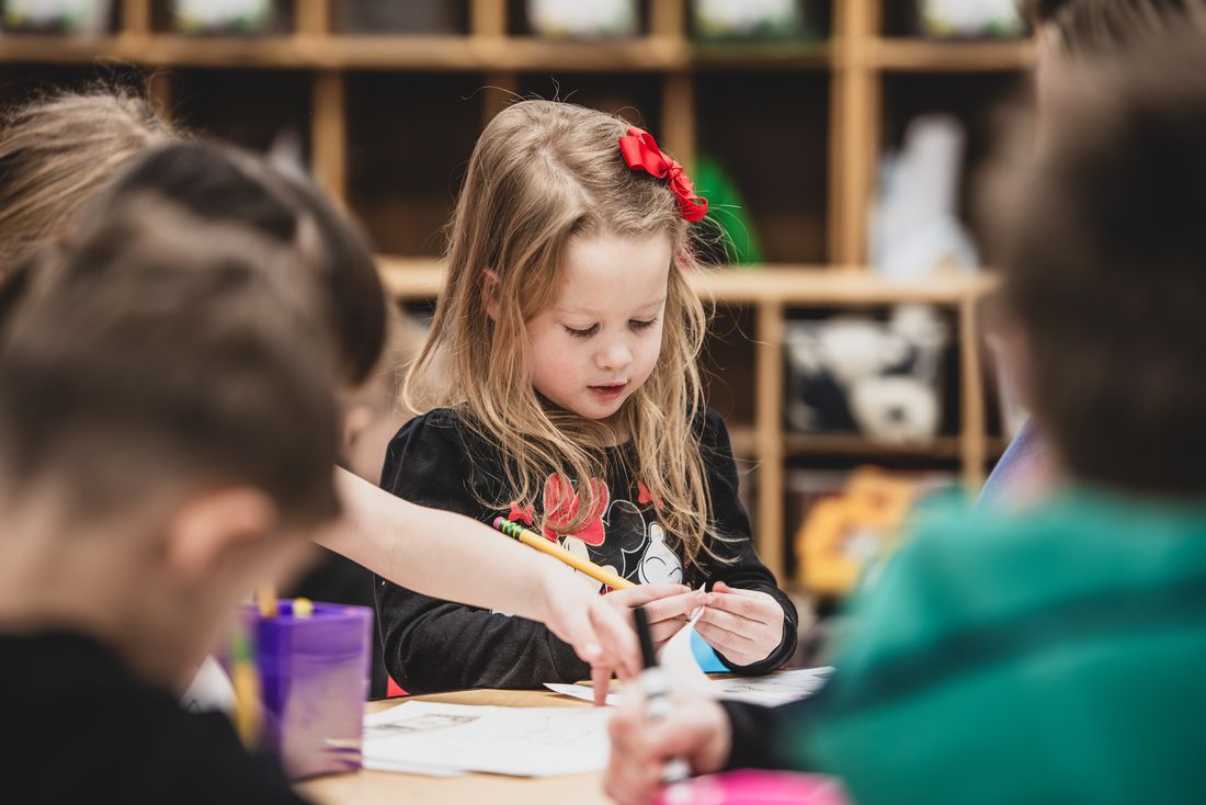 A girl with a red bow writes carefully at a classroom table