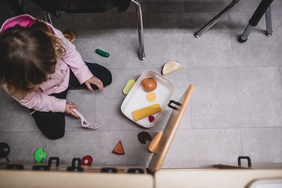 Seen from above, a girl on the floor arranges play food on a tray