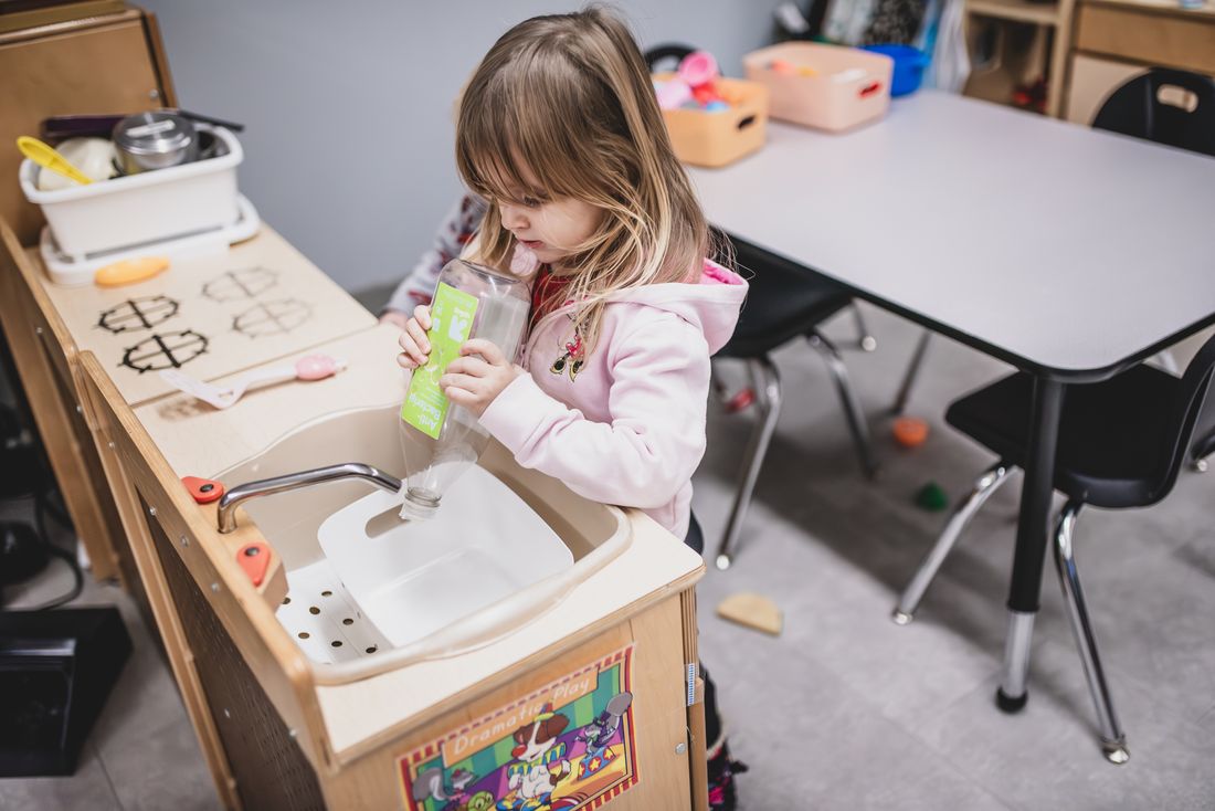 A young girl plays at a wooden play kitchen sink