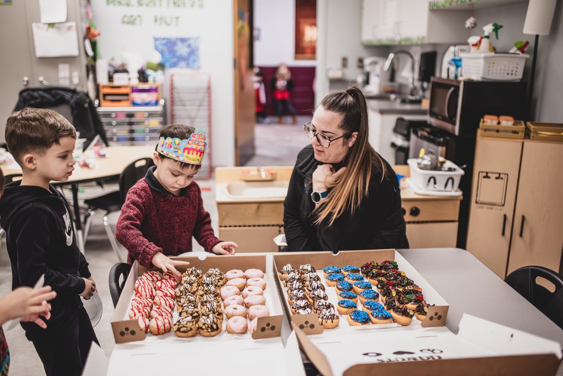 A teacher and two boys look over boxes of decorated donuts for a classroom party