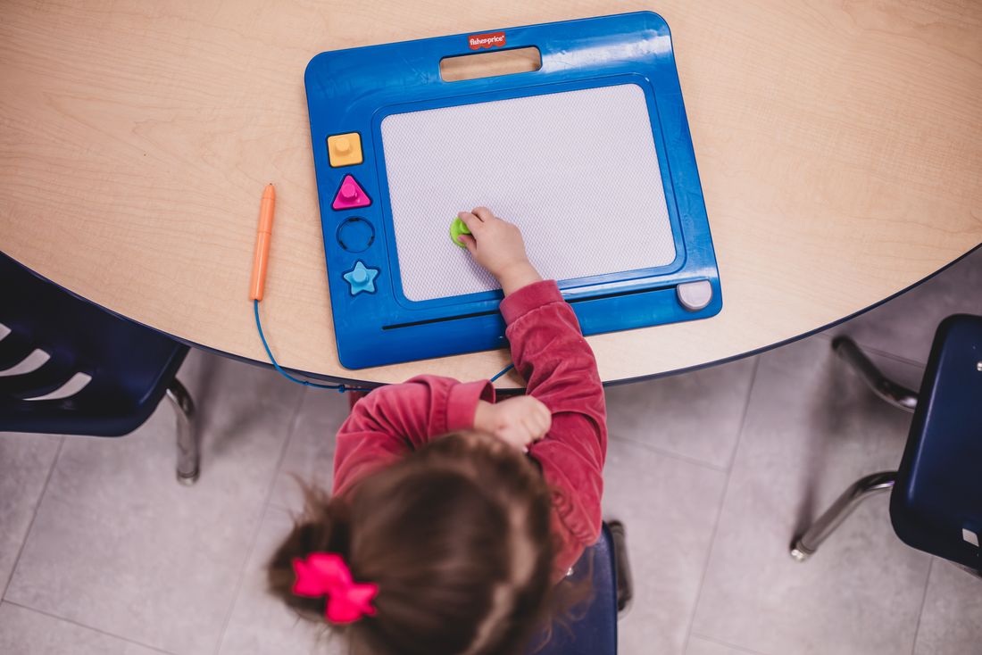 Seen from above, a girl draws on a blue magnetic board at a round table