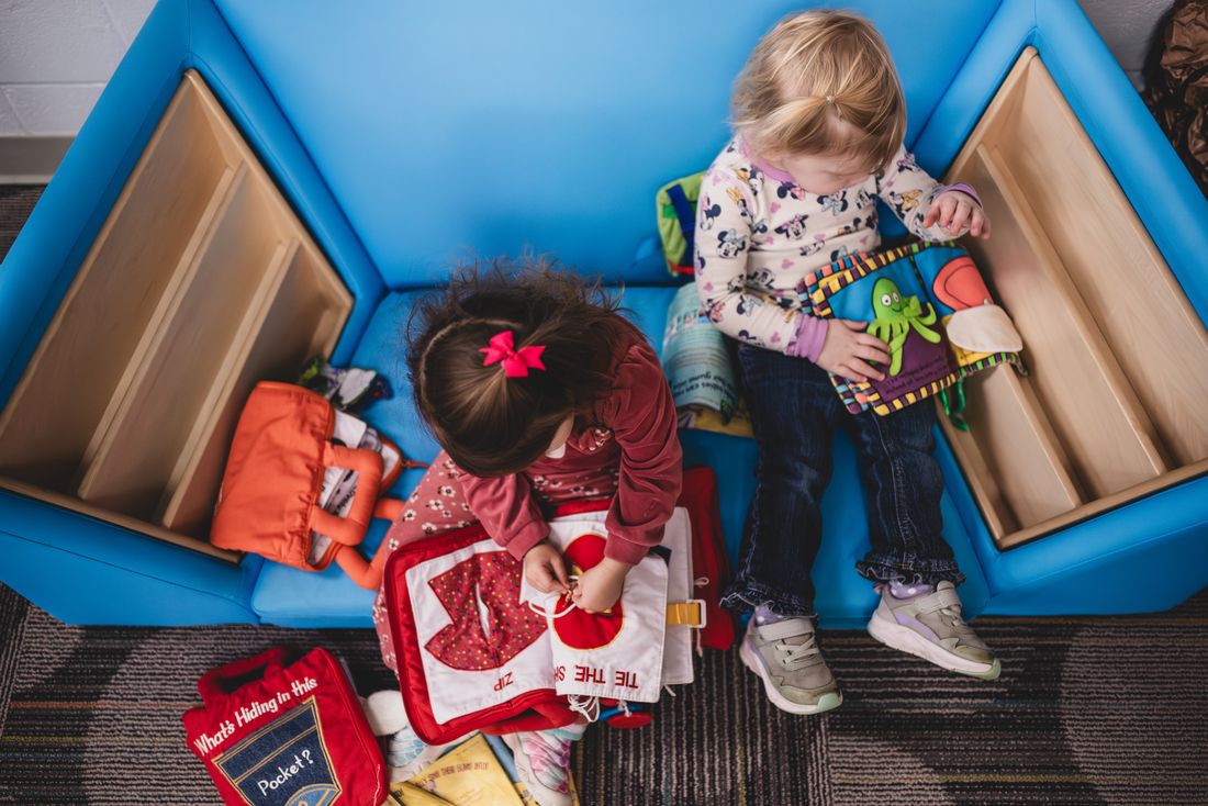Two toddlers explore cloth books in a blue soft-play corner, seen from above
